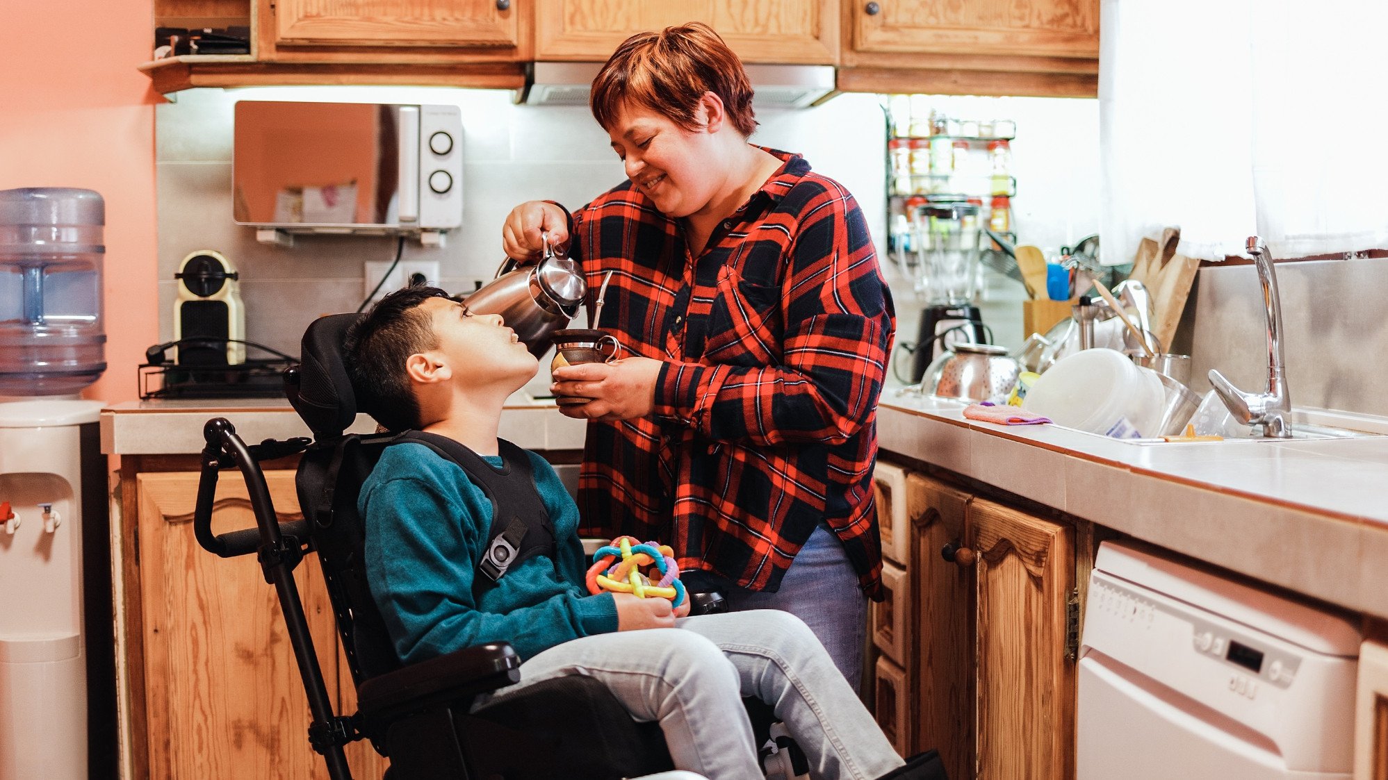 A carer pouring a cup of coffee while talking to a child in an assistive chair